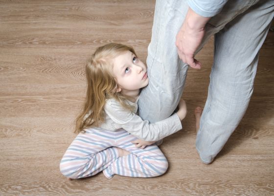 niña con cara triste abrazada a la pierna de un adulto