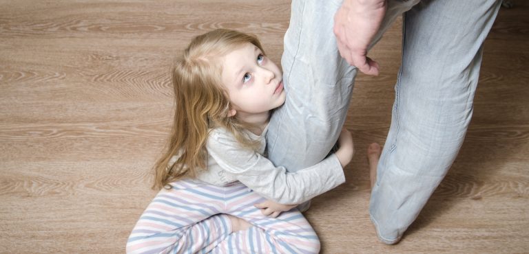 niña con cara triste abrazada a la pierna de un adulto