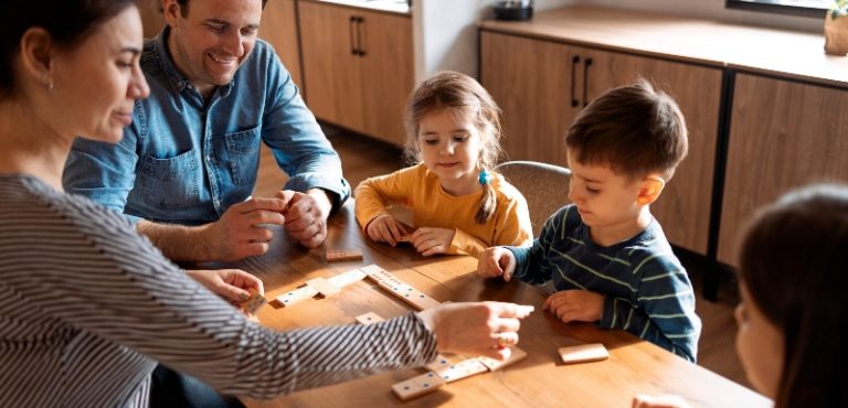 Familia compuesta de padres e hijos jugando dominós